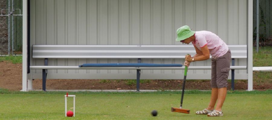 A member in a green hat lining up a croquet shot, ball and hoop in front