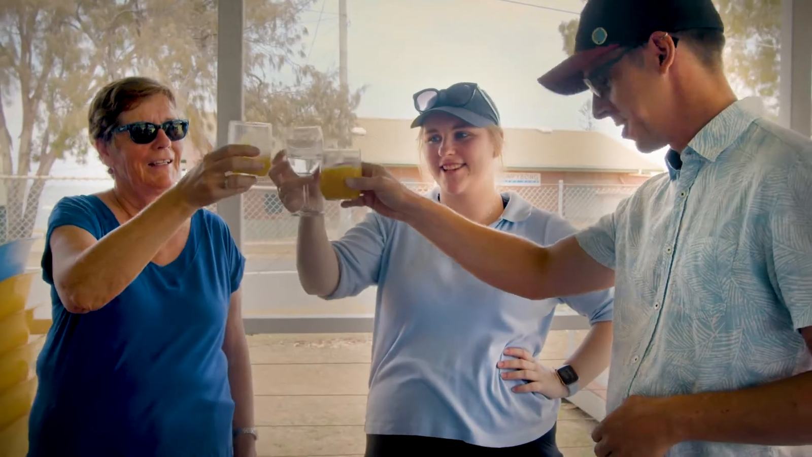 Three players raising glasses of juice on a clubhouse verandah
