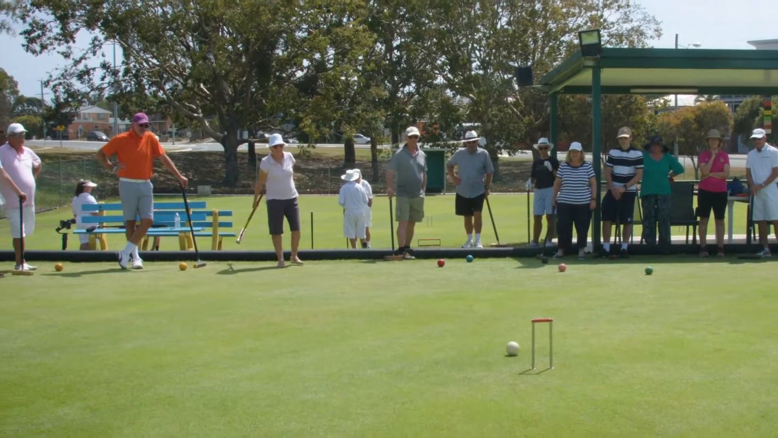 A row of members watching a ball roll towards a hoop on a wide lawn